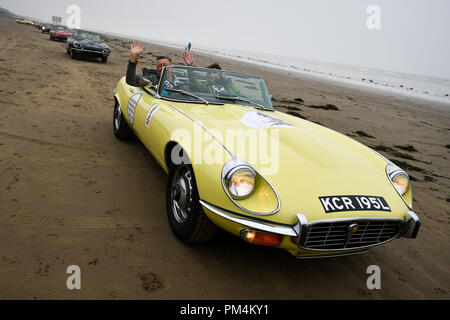 Decine di classici E-type Jaguar a lasciare la spiaggia a Pendine Sands, Carmarthenshire, Galles, come cominciano a coastal intorno al Regno Unito viaggio in aiuto del cancro della prostata carità. Foto Stock