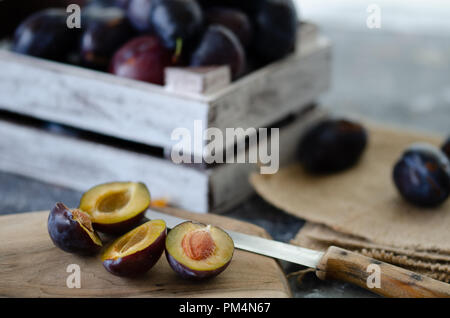 Viola damson prugne su un tavolo di legno. La metà di blu prugna frutto. Molte belle prugne in scatola di legno. Foto Stock