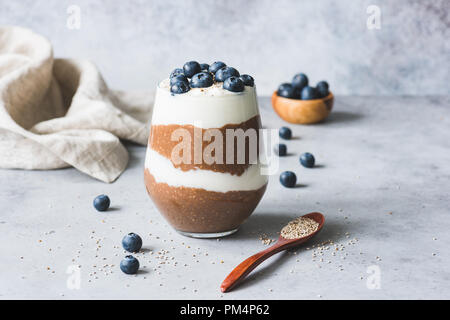 Il cioccolato Chia budino di sementi in vetro e rabboccato con mirtilli su sfondo di calcestruzzo Foto Stock