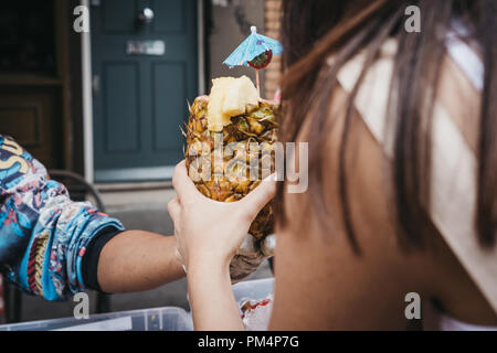 Donna di acquistare un drink tropicale servita all'interno di un ananas fresco a una pressione di stallo di mercato nel mercato di Portobello Road, Londra, Regno Unito. Foto Stock