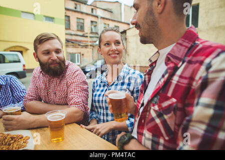 Il gruppo di amici godendo e bere la birra al bar esterno o pub. Bollito di salsicce bianche, servito con birra e salatini. Perfetto per l'Oktoberfest. In legno naturale dello sfondo. Vista anteriore con maschi e femmine di mani Foto Stock