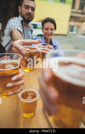 Il gruppo di amici godendo e bere la birra al bar esterno o pub. Bollito di salsicce bianche, servito con birra e salatini. Perfetto per l'Oktoberfest. In legno naturale dello sfondo. Vista anteriore con maschi e femmine di mani Foto Stock