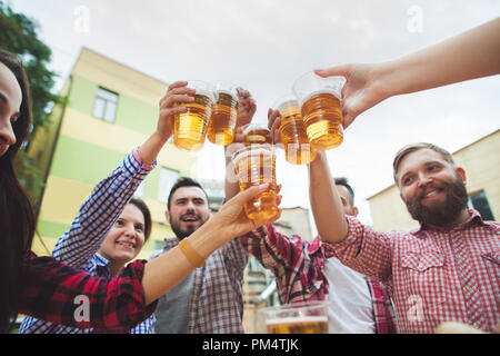 Il gruppo di amici godendo e bere la birra al bar esterno o pub. Bollito di salsicce bianche, servito con birra e salatini. Perfetto per l'Oktoberfest. In legno naturale dello sfondo. Vista anteriore con maschi e femmine di mani Foto Stock