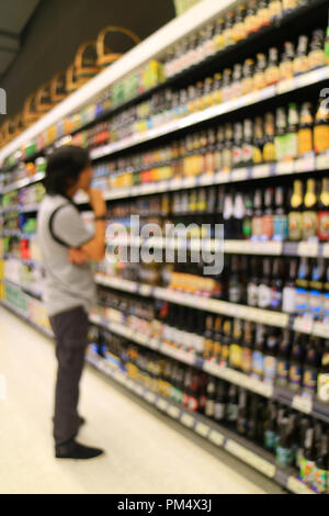 Foto verticale di offuscata giovane scegliendo qualcosa al ripiano di generi alimentari nel negozio al dettaglio Foto Stock