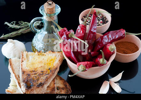 Peperoncino rosso, olio, pane, aglio e pepe in un vaso di argilla Foto Stock