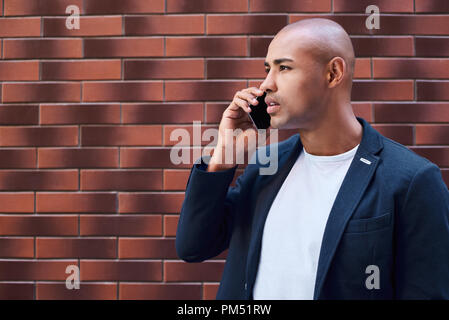 Comunicazioni aziendali. Giovane ragazzo in piedi sulla parete parlando sullo smartphone pensieroso vista laterale di close-up Foto Stock