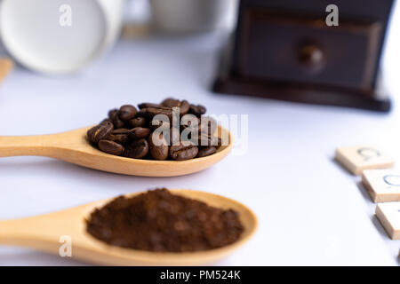 Cucchiai di legno riempito di caffè in grani frantumati e caffè macinato su sfondo bianco Foto Stock