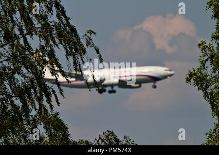 Un aereo bianco con strisce rosse preparazione a terra. Foto scattata attraverso gli alberi, aereo sfocati sullo sfondo. Foto Stock