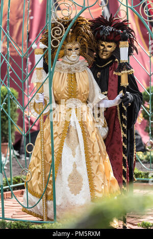 Una donna in bianco e oro veneziano costume di carnevale sorge accanto a un misterioso uomo in nero e oro costume Foto Stock