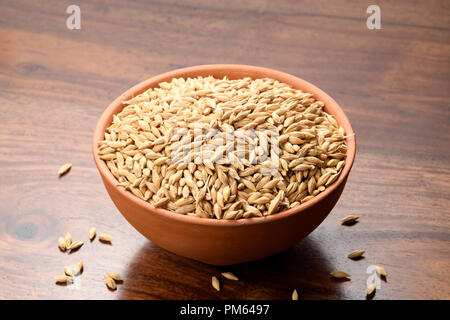 Close up di orzo mondato in un vaso di argilla su sfondo di legno Foto Stock