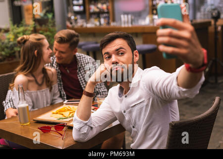 Giovane uomo prendendo selfies pur sentendosi annoiato con gli amici Foto Stock