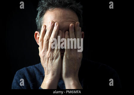 Ritratto di uomo su sfondo nero, ha sottolineato, le mani sul viso Foto Stock