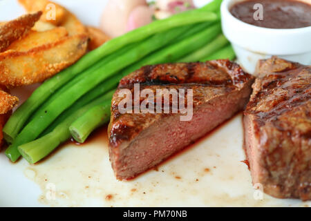 Di medie alla brace bistecca di filetto tagliato a metà con sfocate di verdure cotte al vapore e patate fritte servite sulla piastra bianca Foto Stock