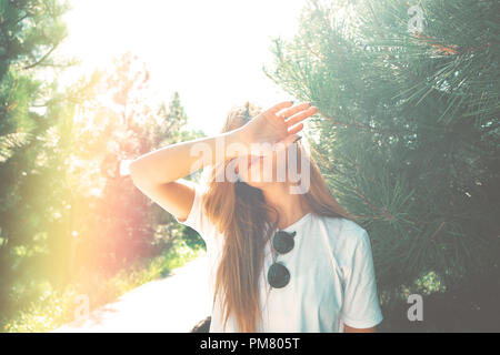 Close-up giovane donna con bel viso dispone di nascondere la sua faccia da raggi solari con braccio, pino in background. I filtri di luce usati. Foto Stock