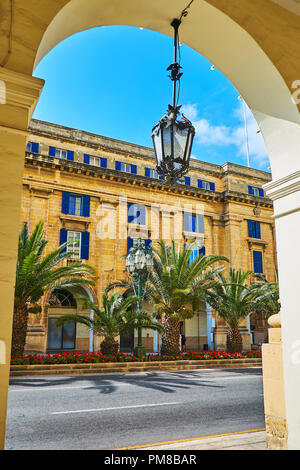 La vista panoramica attraverso l'arco sulle verdi palme ed edificio di pietra a St Anne avenue, Floriana, Malta. Foto Stock