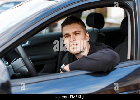Felice giovane uomo seduto in un auto nera Foto Stock