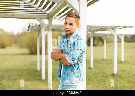 Bel giovane uomo alla moda in jeans abiti sorge nei pressi di una tettoia sulla spiaggia Foto Stock