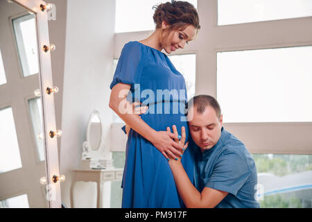 Felice giovane orecchio mettendo a donne in stato di gravidanza womans ventre ascoltando baby spostando all'interno, amorevole marito curioso abbracciando il supporto di gestanti moglie, expe Foto Stock