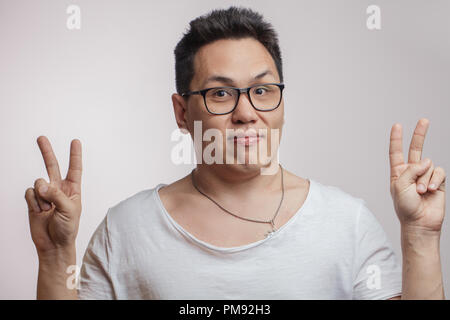 Funny Man coreano in occhiali e t-shirt che mostra segni di pace Foto Stock