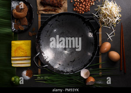 Cibo tailandese di cottura ingredienti con il dado, germogli, uovo, tofu, limone, zucchero, pepe di cayenna, cipolla, banana leaf, bacchette e pan su sfondo scuro. T Foto Stock