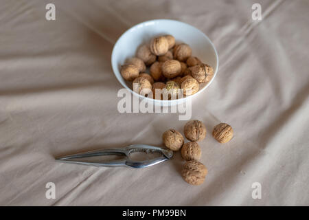 Schiaccianoci e noci in una ciotola su un tavolo ricoperto da una tovaglia. Snack sul tavolo della cucina. Sfondo chiaro. Foto Stock