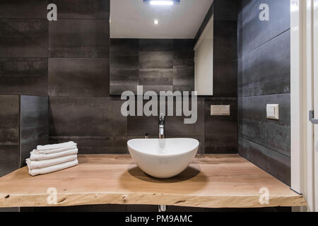 Gli interni moderni del bagno. Il lavello è fatta di bianco guscio massiccia sul tavolo di legno. Minimalismo e semplicità in un grigio brillante interni funzionali. Vista superiore Foto Stock