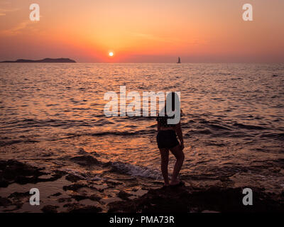 Una giovane ragazza guarda il tramonto sulla baia di San Antonio, Ibiza Foto Stock