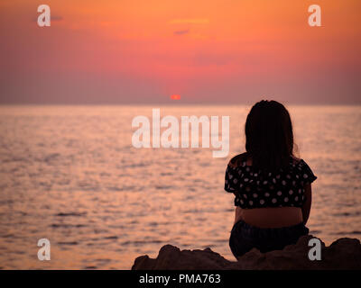 Un giovane giel orologi il tramonto sulla baia di San Antonio, Ibiza Foto Stock