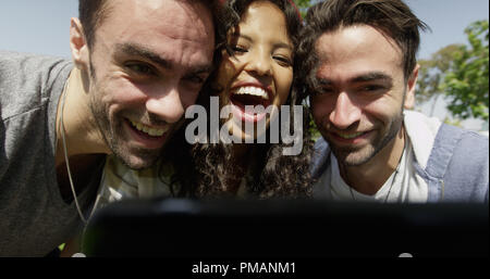 Un gruppo di tre giovani amici multirazziale tenendo selfie presso il parco Foto Stock