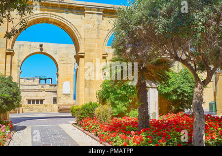 I fiori luminosi e ombreggiata verde di Upper Barrakka Gardens con una vista sulla sua galleria arcuata, Valletta, Malta. Foto Stock