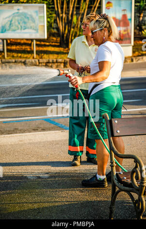 I parchi e i giardini dei lavoratori di sesso femminile con la spruzzatura di acqua al di fuori di un tubo flessibile in Opatija, Croazia Foto Stock