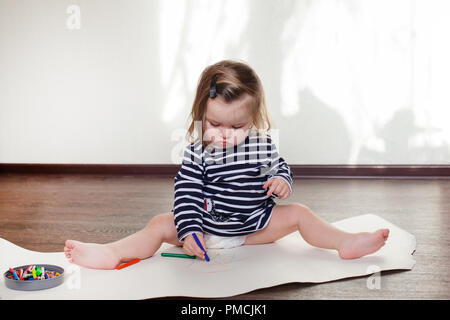 Bambina disegna sul pavimento di una stanza in una giornata di sole Foto Stock