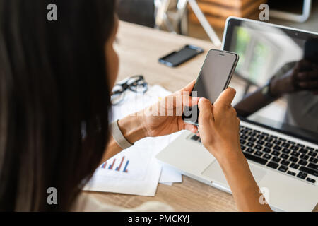La digitazione di messaggi commerciali. Close-up di giovane donna in convenzionale tenendo il telefono cellulare mentre è seduto al suo posto di lavoro Foto Stock