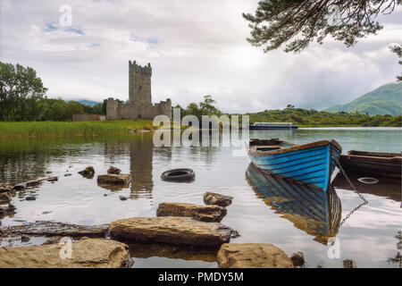 Castello di Ross rovine e il Lough Leane lago con una barca blu in primo piano nel Parco Nazionale di Killarney, Irlanda Foto Stock