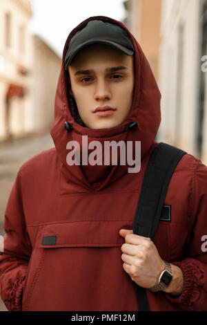 Bel giovane ragazzo in sportivo giacca rossa con un cappello e una borsa nera sulla strada Foto Stock