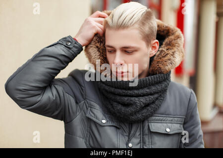 Elegante uomo bello con un taglio di capelli in un quartiere alla moda di Calda giacca invernale con pelo sulla strada Foto Stock