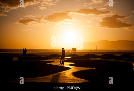 I pattinatori si stagliano contro il sole al tramonto in un esterno di skate park in Venice Beach, Los Angeles, California, USA. Foto Stock