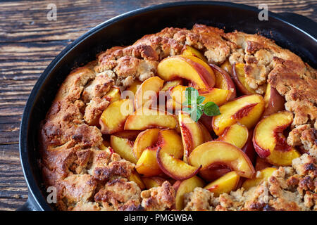 Close up di deliziosi dessert meridionale peach cobbler cotta in un piatto nero, presentato sul vecchio tavolo in legno Foto Stock