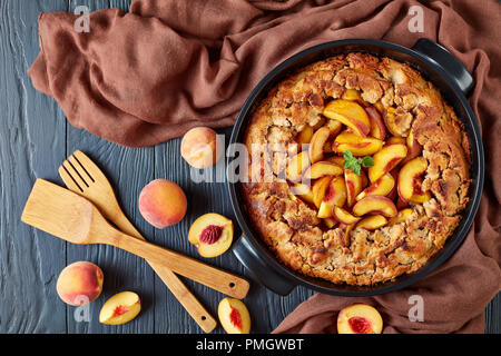 Vista da sopra di un vecchio Peach Cobbler servita con fresche e mature le pesche, insieme con cucina strumenti in legno: un Turner-Spatula scanalato e a f Foto Stock