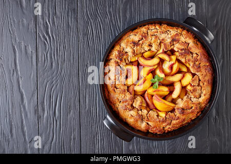 Semplice e sano cobbler pesche cotte in un nero teglia, su tavoli in legno nero, vista dall'alto, laici piatta Foto Stock