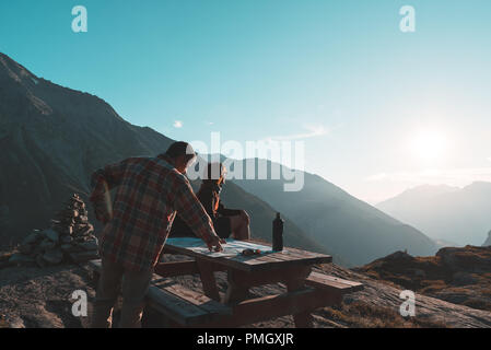 Gli escursionisti Coouple lettura mappa trekking sulla tavola in controluce, vista posteriore. Esplorazione e Avventura sulle Alpi. Foto Stock