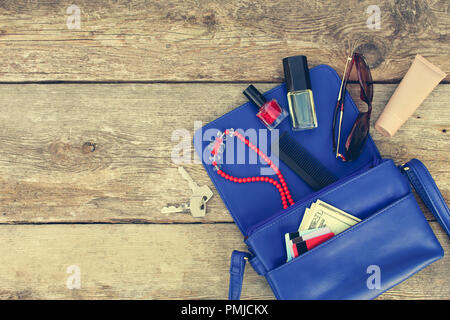 Cose da aprire lady borsa. Cosmetici, soldi e donna accessori è caduto fuori borsa blu. Vista dall'alto. Tonica immagine. Foto Stock