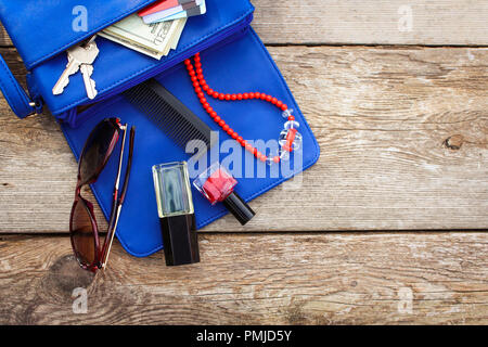 Cose da aprire lady borsa. Cosmetici, soldi e donna accessori è caduto fuori borsa blu. Vista dall'alto. Foto Stock