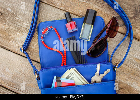 Cose da aprire lady borsa. Cosmetici, soldi e donna accessori è caduto fuori borsa blu. Vista dall'alto. Foto Stock