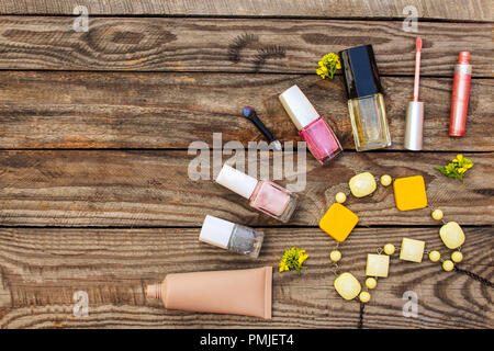 Cosmetici:, ciglia finte, correttore, smalto per unghie, profumo, lucidalabbra, perline e fiori di colore giallo su sfondo di legno. Tonica immagine. Foto Stock