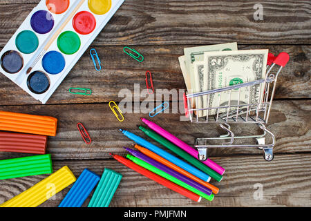 Carrello con denaro. Ufficio e forniture scolastiche sul vecchio sfondo di legno. È un concetto di acquistare oggetti di cancelleria. Foto Stock