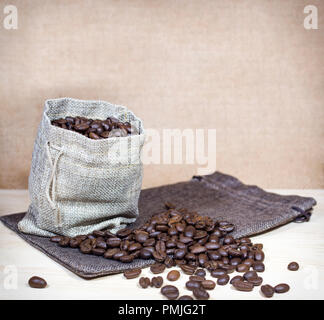I chicchi di caffè nel sacco di tela e i chicchi di caffè sparsi in superficie. Foto Stock