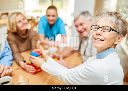 Donna senior con demenza e amici a giocare con colorati mattoni per costruire una casa di riposo Foto Stock