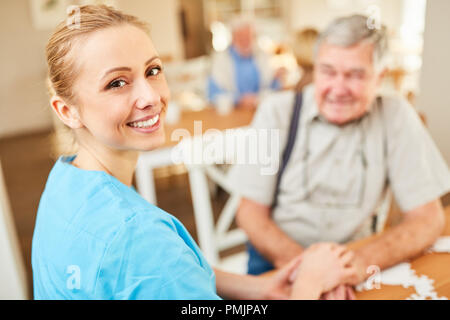 Il caregiver sorridente donna o infermiera geriatrica comfort un senior in condizioni di vita assistita Foto Stock