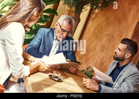 Pranzo di affari. Tre persone al ristorante seduti al tavolo per discutere il progetto gioiosa di close-up. Lavoro di squadra concetto Foto Stock